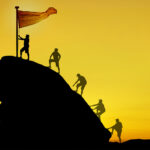 group of leaders planting a flag at the top of a hill.